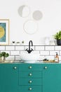 Turquoise cupboard, sink, black faucet and round mirror in a modern bathroom interior. Real photo