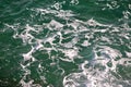 Turquoise green seawater with sea foam as background, close up. Surface of sea with waves, splash, foam and bubbles.