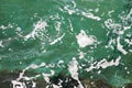 Turquoise green seawater with sea foam as background, close up. Surface of sea with waves, splash, foam and bubbles. Royalty Free Stock Photo