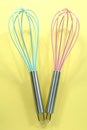 Turquoise and pink kitchen whisks on yellow background Royalty Free Stock Photo