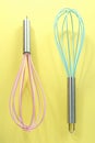 Turquoise and pink kitchen whisks on yellow background Royalty Free Stock Photo