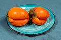 Turquoise plate with two ugly orange persimmons on dark turquoise textile napkin close up.
