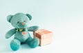 Turquoise soft teddy bear with an embroidered heart holds a gift box and a bow on a blue background. Children`s toy. Love, a gift