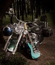 Turquoise Stratocaster electric guitar leaning on Harley Deluxe motorcycle in the woods