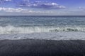 Turquoise Swells crashing into black pebbled beach on a blue sky summer day in Sicily