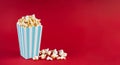 Turquoise white striped carton bucket with tasty cheese popcorn, isolated on red background