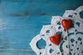 Turquoise wooden background in country style with two red hearts on crocheted lace doily