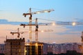 Turret slewing cranes with light on frame working at sundown at evening time, buildings under construction Royalty Free Stock Photo