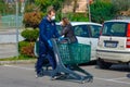 A young coucasian male with white face mask strolling in parking lot with shopping cart. Buying groceries in pandemic in Italy