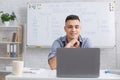 Tutor evaluates students knowledge. Young man looking at laptop in classroom