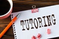 TUTORING - word on a white sheet on a wooden brown background with a cup of coffee and a pen