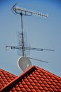 TV antennas and satellite dish for television mounted on the tiled roof of house isolated on blue sky background in countryside Royalty Free Stock Photo