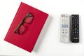 TV remote control, red book and glasses on white coffee table