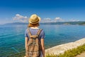 Tween tourist girl in hat and backpack admiring beautiful landscape of lake Baikal from waterfront of Listvyanka village in sunny Royalty Free Stock Photo