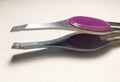 Tweezers with purple handle on white background.