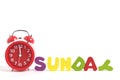 Twelve clock on red alarm clock and word Sunday made up letters white background.