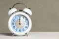 Twelve o'clock on the alarm. A white alarm clock is on a white table. The clock hand points to 12 o'clock. Time Royalty Free Stock Photo