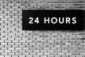 Twenty four hours glowing sign on brick wall, black and white s