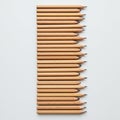 Twenty sharpened wooden pencils are uniformly arranged in parallel rows on a plain white surface. Royalty Free Stock Photo