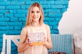 Twenty-year-old blonde woman sitting on a bench in the room and holding a beautiful box Royalty Free Stock Photo