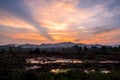 Twilight dramatic sky with orange sunlight all over the sky, with silhouette of mountains, trees and marsh on the foreground. Royalty Free Stock Photo