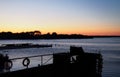 Twilight over a lake with the sun setting behind a tree covered island with glowing orange sky and a jetty and old paddle boat in Royalty Free Stock Photo