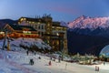 Twilight townscape of Gorky Gorod mountain ski resort on snowy Chugush mountain peak background. People on snowy slope at night sk