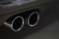 Twin chrome tailpipe of powerful sports car with black body and gray plastic parts