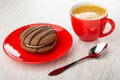 Twin cookie with cream filling in saucer, cup of black coffee, spoon on wooden table Royalty Free Stock Photo