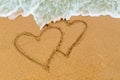 Twin double heart drawn on sandy beach with wave approaching Royalty Free Stock Photo