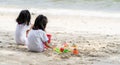 Twin girls while playing beach toys and sitting on a beach sand with white sand and waves Royalty Free Stock Photo