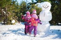Twin girls in the winter in the woods for a walk near a large snowman. Children in pink jackets and glasses in the sun jumping