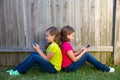 Twin sister girls playing smartphone sitting on backyard lawn