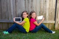 Twin sister girls playing tablet pc sitting on backyard lawn