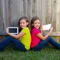 Twin sister girls playing tablet pc sitting on backyard lawn Royalty Free Stock Photo