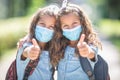 Twin sisters with face masks go back to school during the Covid-19 quarantine and showing thumbs up Royalty Free Stock Photo