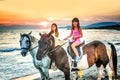 Twin sisters riding horses in the sunset by the sea on the isla Royalty Free Stock Photo