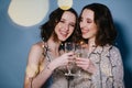 Twin sisters in shiny evening dresses celebrate with glasses of sparkling wine Royalty Free Stock Photo