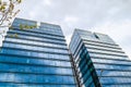 Twin skyscrapers with glass windows on a stormy day with clouds reflecting blue on the exterior of the buildings.