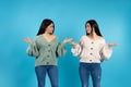 Twin women spread their palms to the sides looking at each other. Emotions for your advertisment on blue background