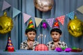 Twins adorable boy in shirt, celebrating his birthday, blowing candles on homemade baked cake, indoor. Birthday party for kids Royalty Free Stock Photo