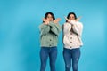 Twins, brunettes in the same clothes on a blue background, crossed their arms, showing stop. Side space.