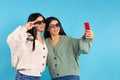 Twins in 3D glasses are smiling, posing and taking selfies on a smartphone. Modern technologies on a blue background. Royalty Free Stock Photo