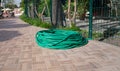 Twisted green rubber hose for watering plants lying on sidewalk
