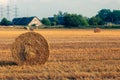 A twisted haystack into a roll closeup and a farm in the distance