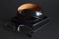 Twisted men`s leather belt in black in a box and eyeglasses on dark background, elegant accessories Royalty Free Stock Photo
