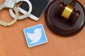 Twitter paper logo lies with wooden judge gavel, smartphone and handcuffs. Entertainment lawsuit concept
