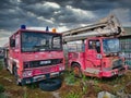 Two abandoned, rusting, derelict fire engines with fading paintwork, one Dennis and the other Dodge