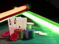 Two aces standing leaning on chips piles, some of them laying nearby on green cover of playing table, under green and