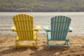 Two adirondack chairs on the sandy beach by the lake